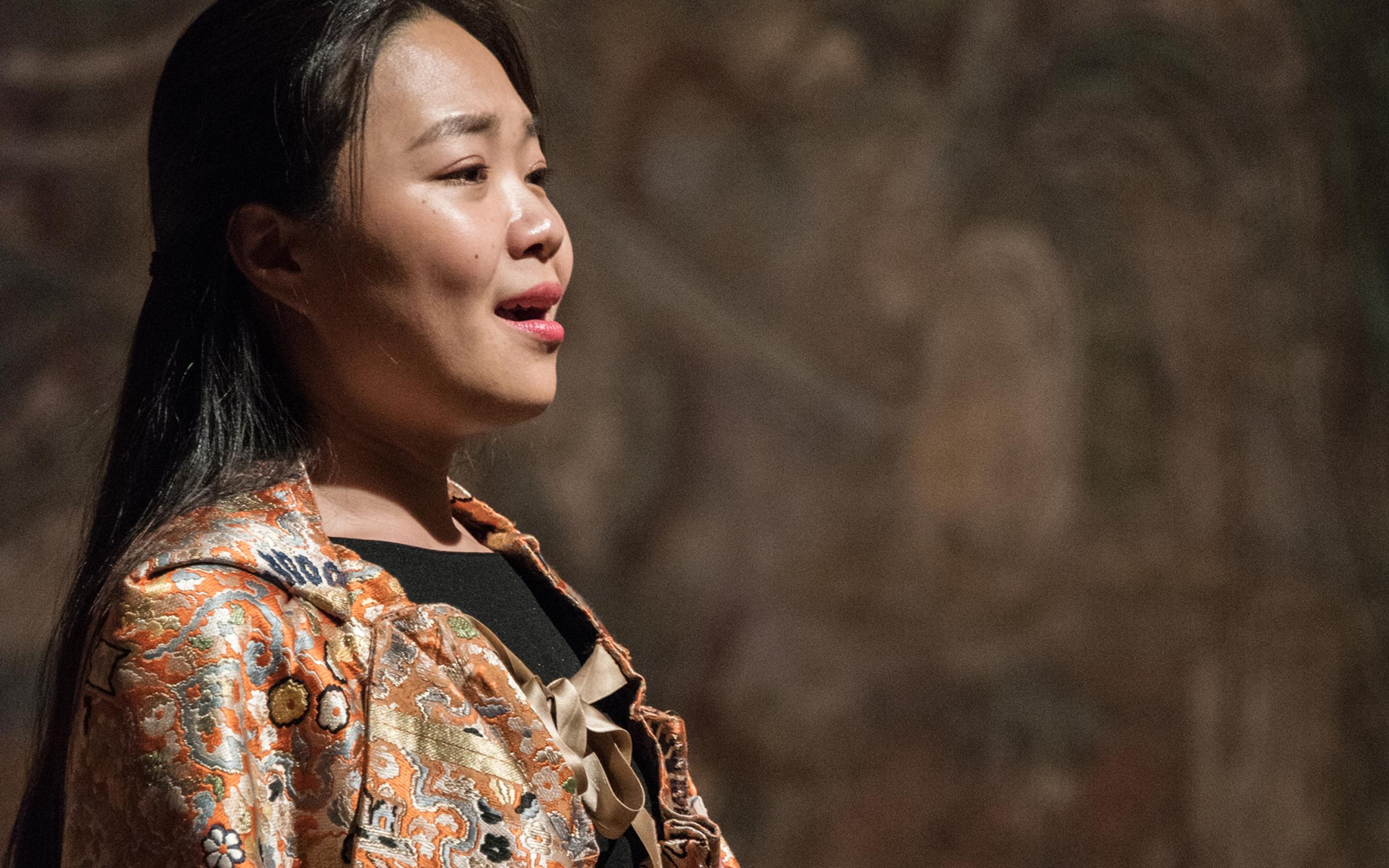 A performer sings while wearing a robe embroidered with gold, orange, and blue designs.