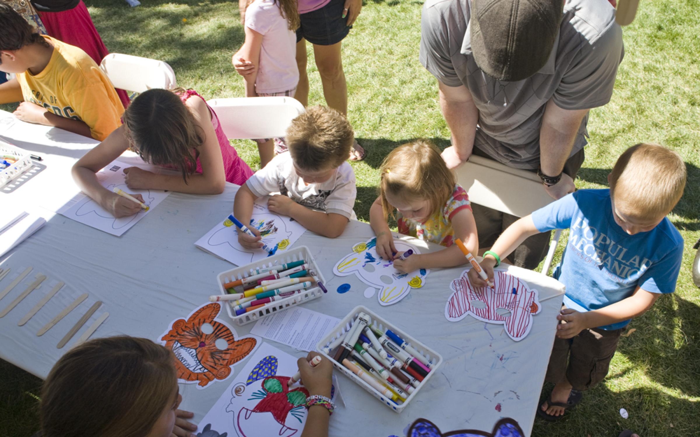 An aerial photo of a group of children coloring masks while gathered around a table.