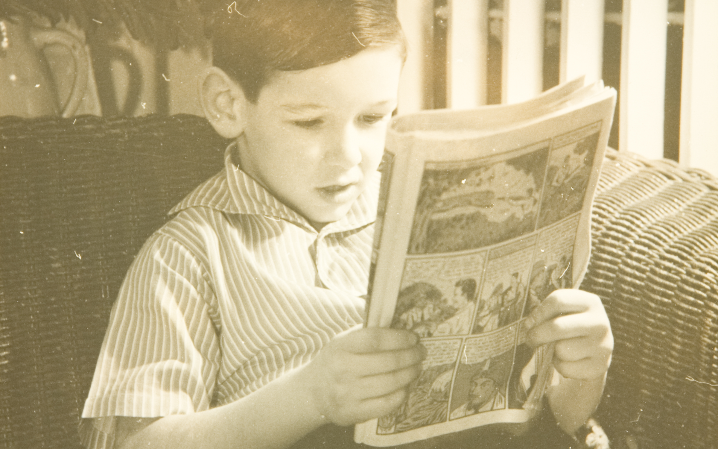 A black and white photo of a young boy reading a comic book. 