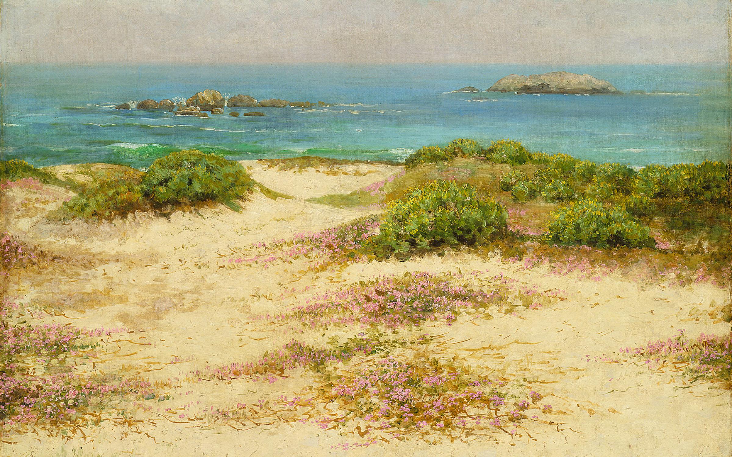 A beach scene with patches of grass in the sand. Rocks protrude from the ocean in the background.