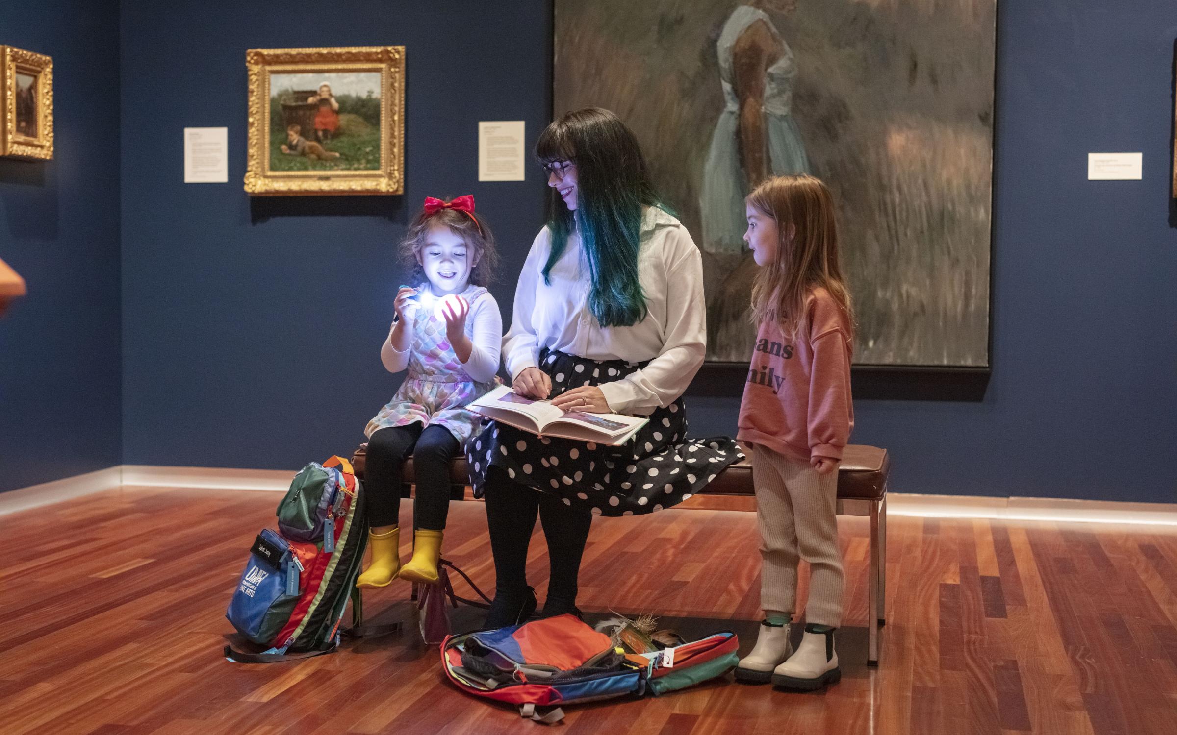 A family explores a gallery at UMFA with provided family backpacks to enhance their experience.