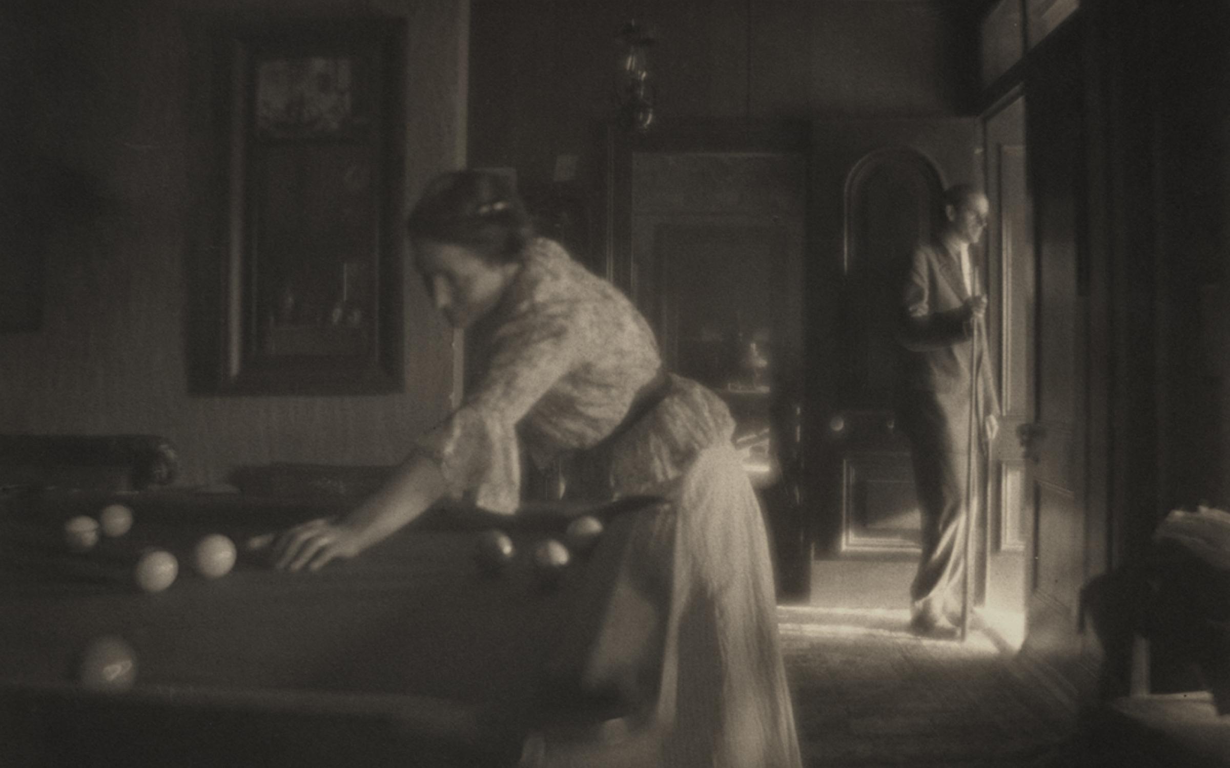 A black and white photograph of a woman playing billiards.