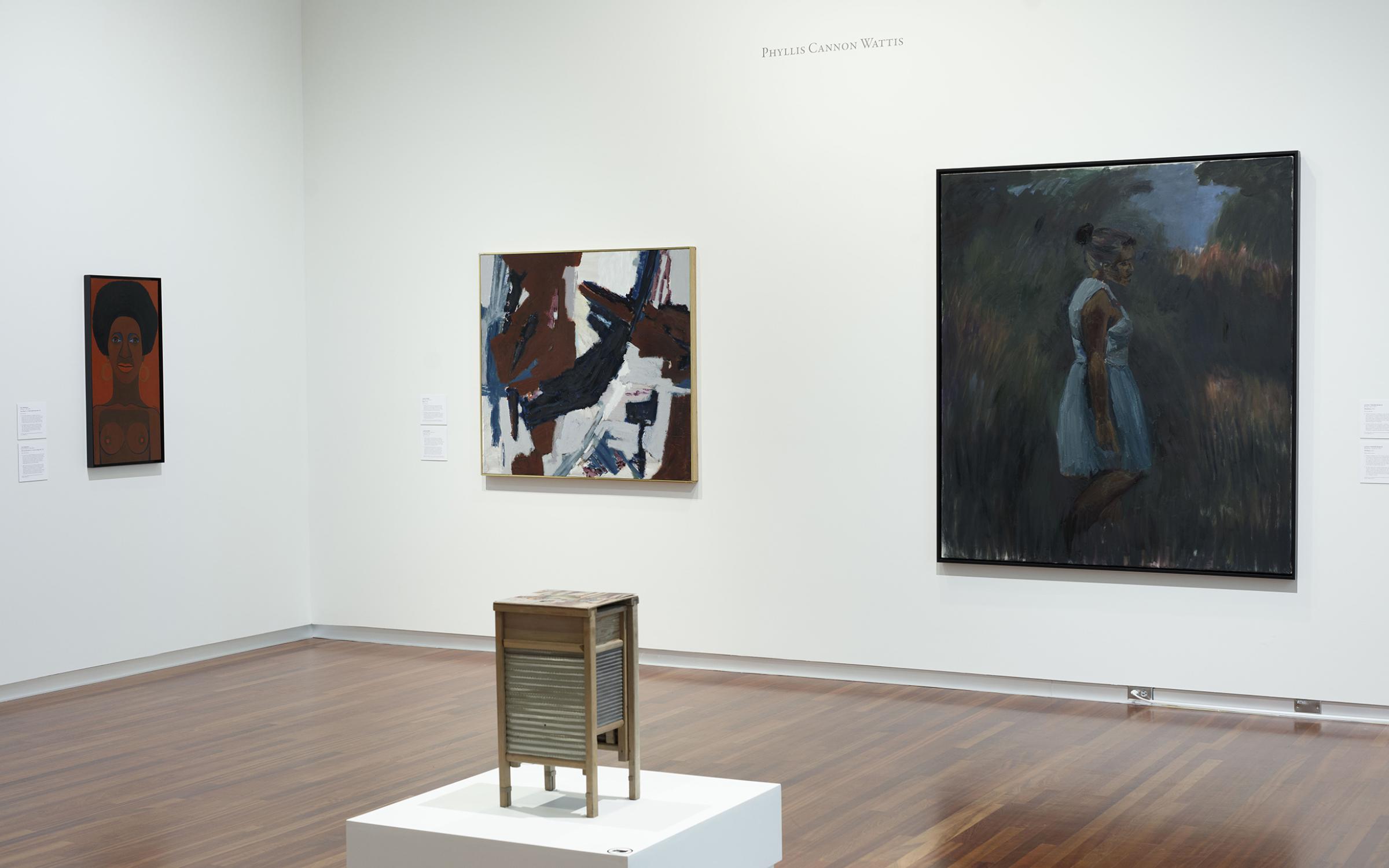 Two painted canvas hanging on a white wall behind a small wooden table.