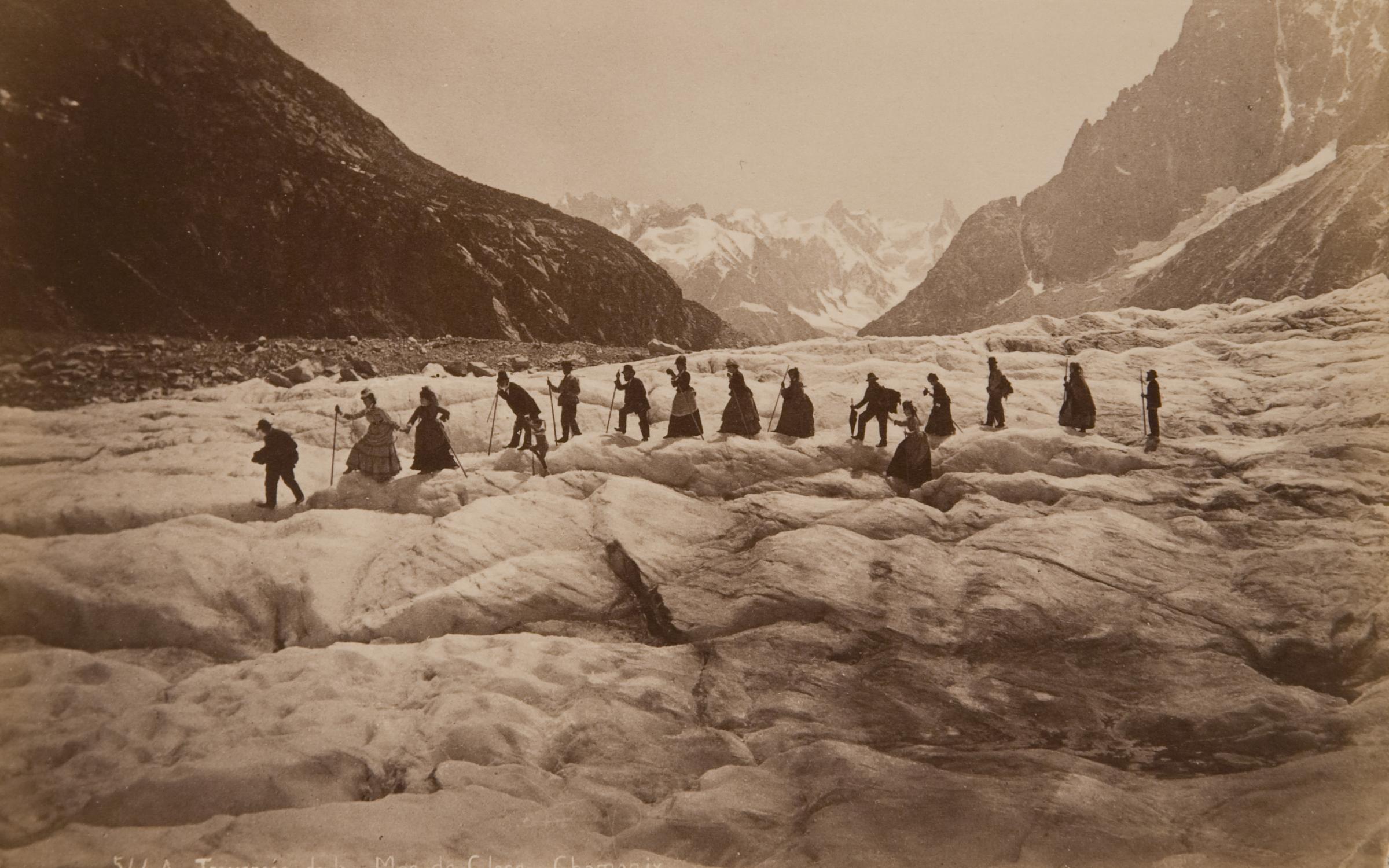 A black and white photograph of a group of people hiking over a glacier.