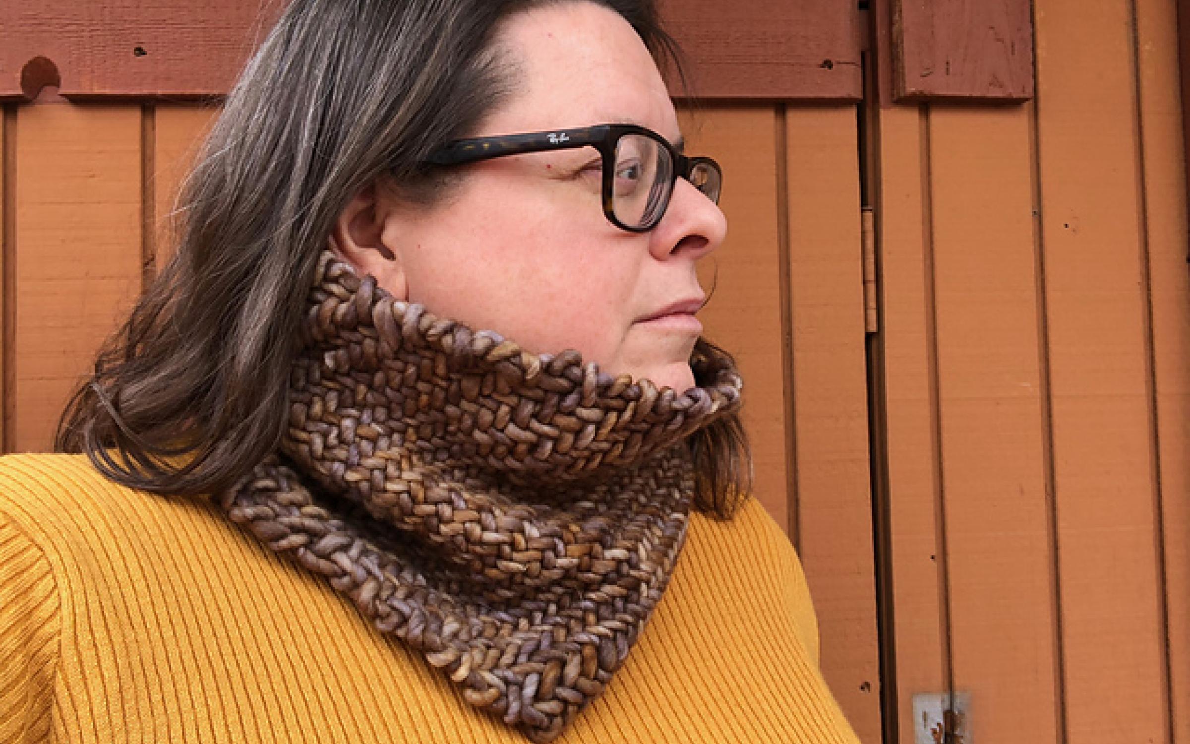 A woman in a yellow shirt models a woven cowl.