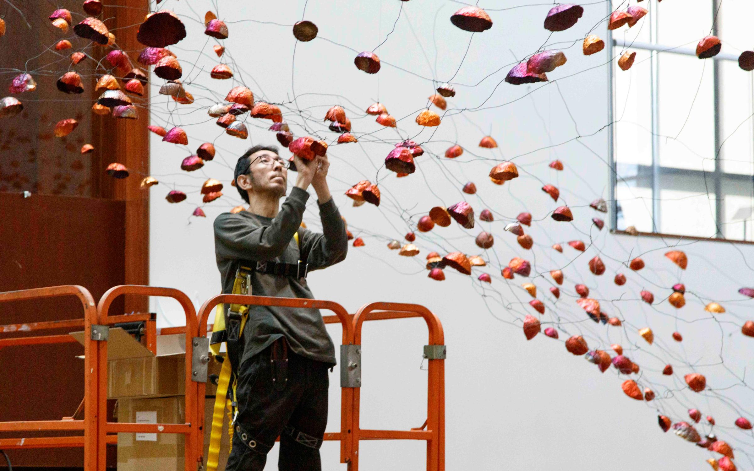 Installation of "Stone on Boundary" Artist Onishi Yasuaki attaches a copper bowl to a net of wires.