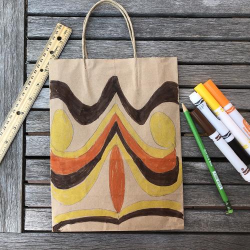 paper bag with orange, yellow and brown wavy lines on it surrounded by a ruler, pencils and colored markers