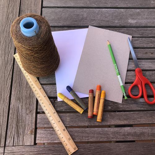 A wooden table with leaf rubbing supplies, a spool of twine, white paper, a small sheet of cardboard, a ruler, five crayon in various colors, a pencil and scissors.
