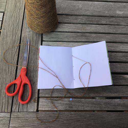 folder white paper with a needle and twine laying on top. red handled scissors sit on table to the left