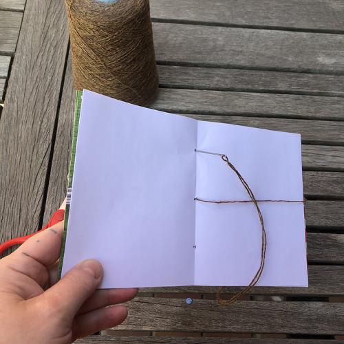 leaf Rubbing book held in a hand is open to center pages a needle is pking through the top hole in the spine with twine dangling from it