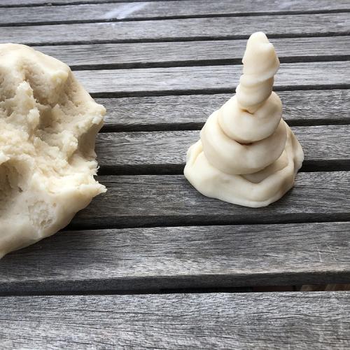a mound of salt dough sits on a wood table next to a cone-like spiral of salt dough