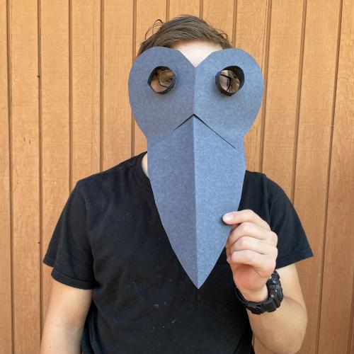 a child in a black shirt hold up a black craft paper plague doctor mask