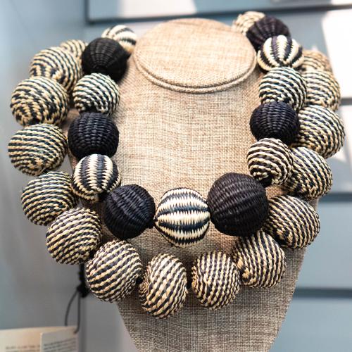 a large statement necklace made of raffia grass woven balls in black and white stripes 