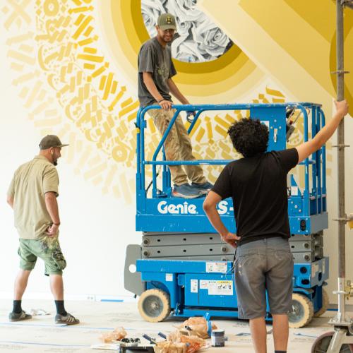 Three artists stand in front of a mural in progress.