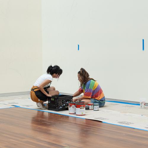 Two people sit on the floor in front of a blank wall, planning.