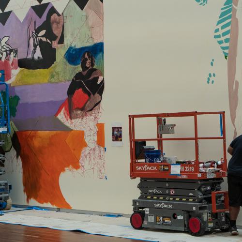 Artists work on large colorful murals.