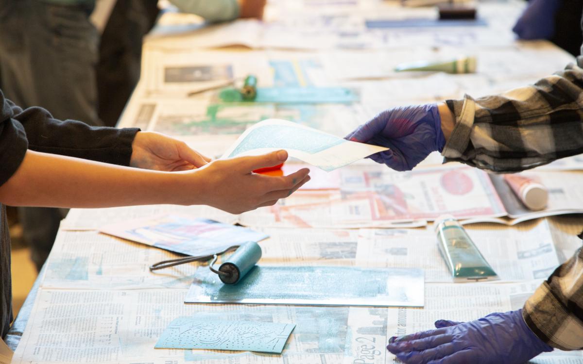A pair of hands accepts a blue print from gloved paint covered hands.