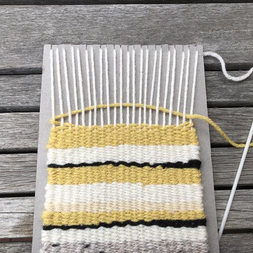 A close up of the woven rug shape and the yellow yarn being woven above and bleow the vertical strips of white yarn.