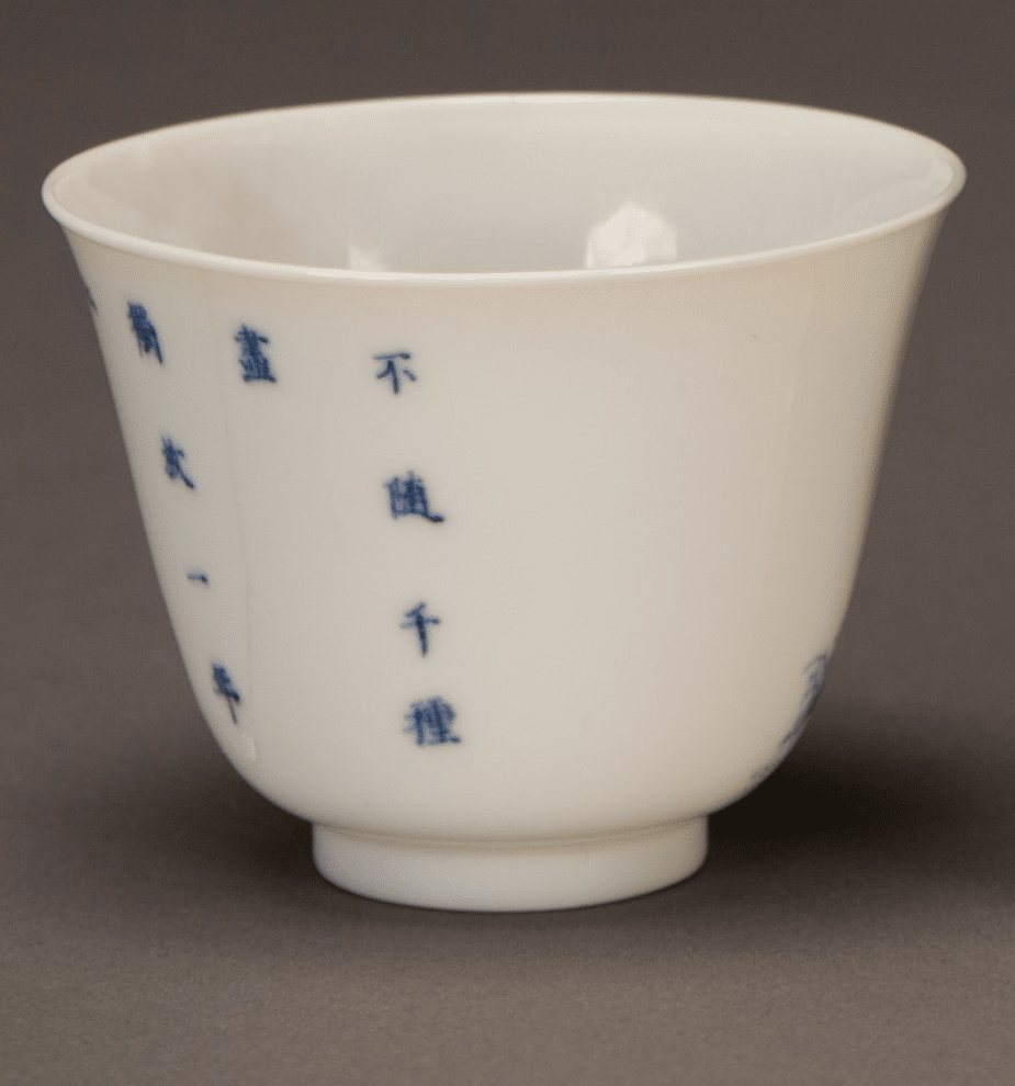 A small white porcelain cup with blue Chinese characters vertically inscribed on its surface, displayed against a neutral gray background.