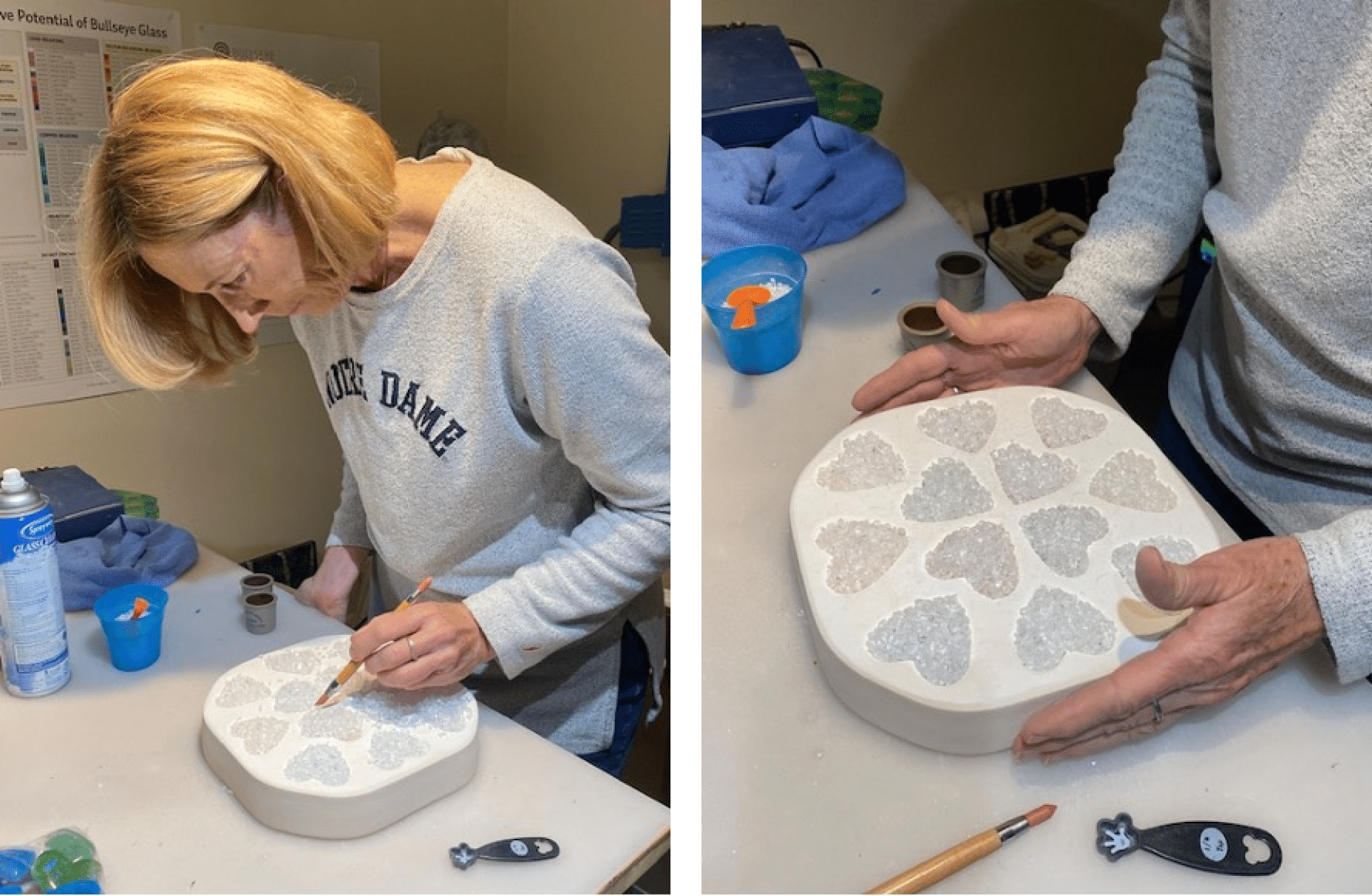 A woman in a gray Notre Dame sweatshirt paints heart-shaped designs in a white tray, using a small brush at a crafting table with tools and supplies. Close-up shows her hands adding color to the heart shapes.