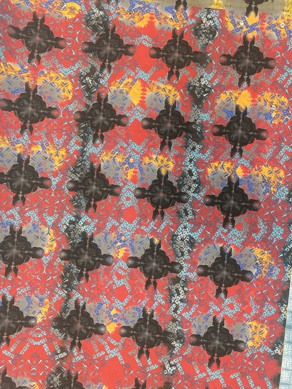 A patterned surface with repeating black silhouettes of a seated figure over a vibrant red, orange, and blue geometric and abstract background. The design is colorful and visually complex.