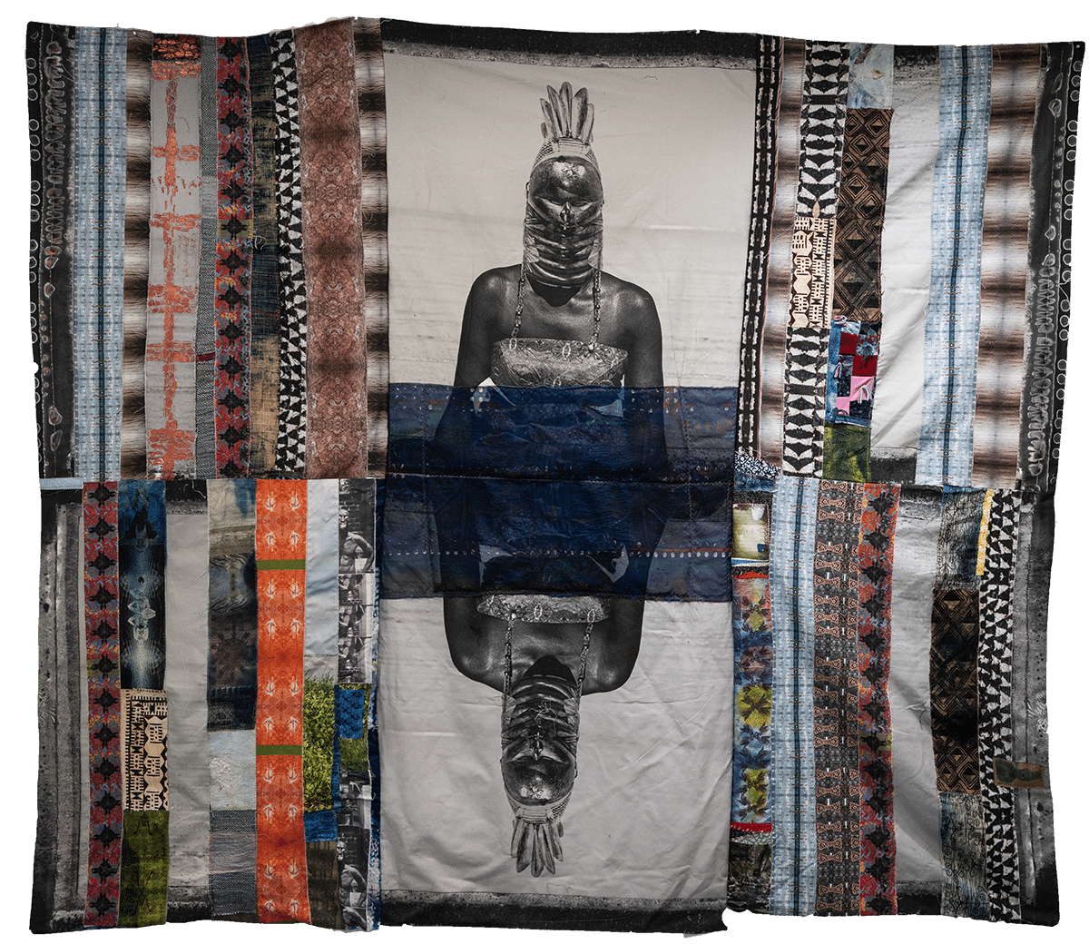 A quilt with colorful, patterned vertical strips, featuring a central black-and-white mirrored image of a person wrapped in fabric, with their face obscured and hand raised above their head.